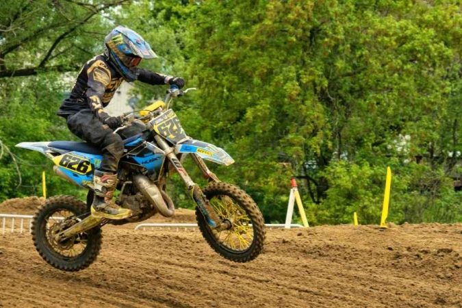 Un pilote de motocross numéro 626 sur une moto bleue et jaune prend de la vitesse sur une piste en terre, illustrant les avantages de la moto en compétition off-road.