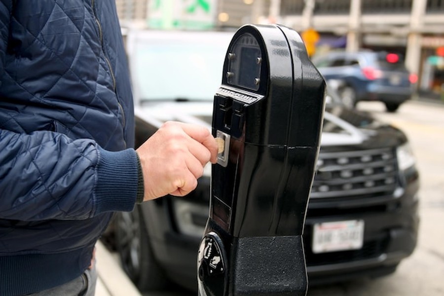 Un homme insère une pièce dans un parcmètre de ville, un geste du quotidien pour les conducteurs qui cherchent aussi à savoir comment brancher sa maison sur la batterie de sa voiture électrique.