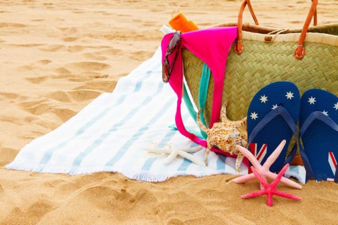 Fouta de plage blanche à rayures bleues étalée à côté d'un panier en osier, de tongs et d'étoiles de mer.