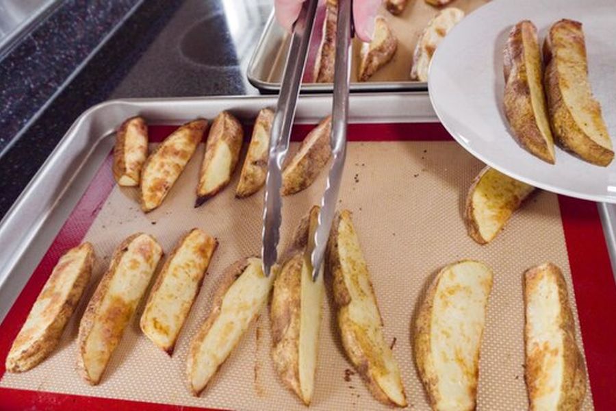 Des quartiers de pommes de terre croustillants disposés sur un tapis de cuisson, parfaits pour apprendre à transformer son Air Fryer en déshydrateur pour créer des snacks sains et économiques.