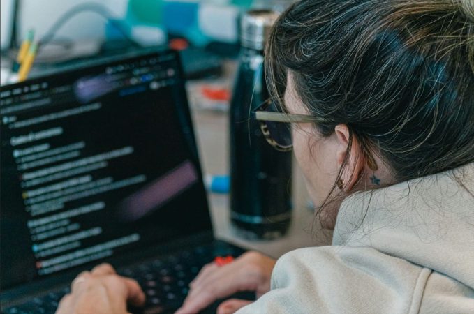 Plan rapproché de dos d'un apprenant portant des lunettes et une veste beige, utilisant un ordinateur portable dans un espace de travail flou, illustrant le concept d'éducation sur mesure avec IA.