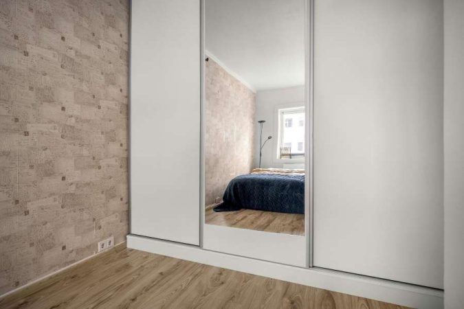 Une armoire de chambre blanche avec une grande porte coulissante centrale démontrant l'importance des miroirs pour agrandir l'espace.
