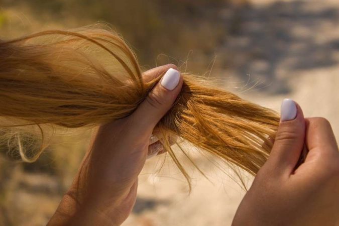Des mains inspectent des cheveux secs et abîmés au soleil.