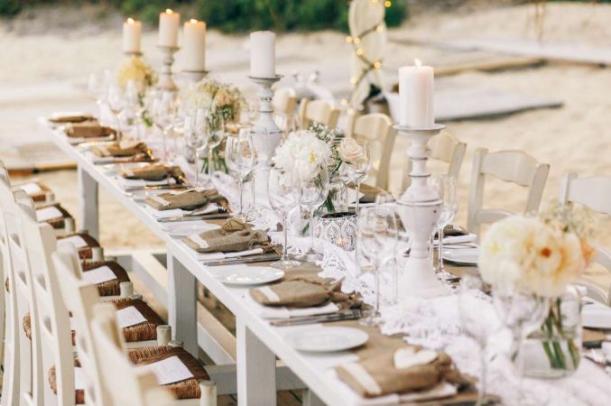 Table de banquet extérieur avec bougeoirs patinés, chemin en dentelle et pochettes en toile de jute, belle idee deco mariage champetre chic vintage.