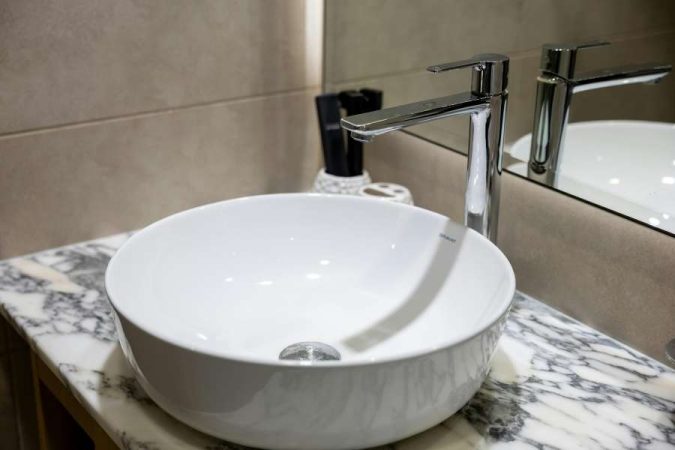 Vasque à poser ronde en céramique blanche installée sur un plan de travail en marbre, accompagnée d'un mitigeur de lavabo chromé élégant.