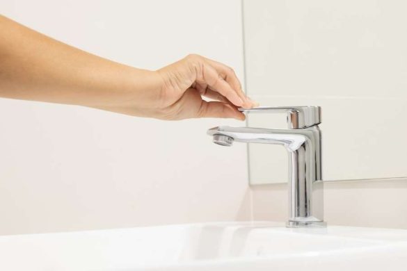 Gros plan sur une main manipulant la poignée d'un mitigeur de lavabo chromé installé sur un meuble de salle de bain blanc.