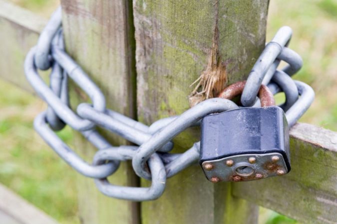 Une grosse chaîne métallique maintenue par un cadenas rouillé faisant office de serrure de portail extérieur sur une barrière en bois.